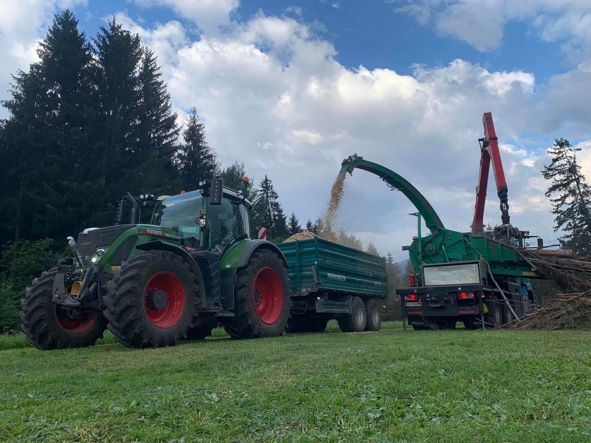 Ein grüner und roter Traktor zieht ein Holzhaus .