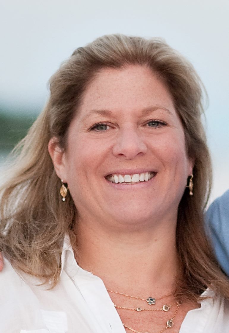 A woman wearing a white shirt and earrings is smiling for the camera.