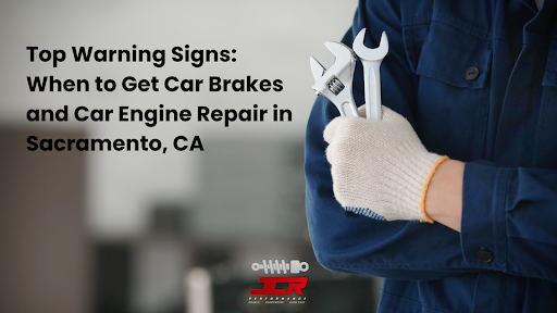 A mechanic in a blue uniform holds a wrench and an adjustable spanner, wears a safety glove and stands in a garage.