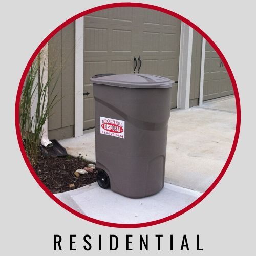 A brown residential trash bin with a disposal company sticker sits on a concrete driveway in front of a garage.