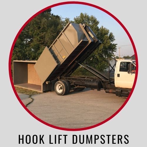 A truck lifting a large, tan metal dumpster container onto its bed, outdoors against trees, titled Hook Lift Dumpsters.