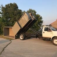 A white dump truck tilting its large, metal dumpster container onto the pavement.