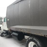 A white dump truck parked in snowy conditions, with icicles hanging from the bottom of the truck bed.