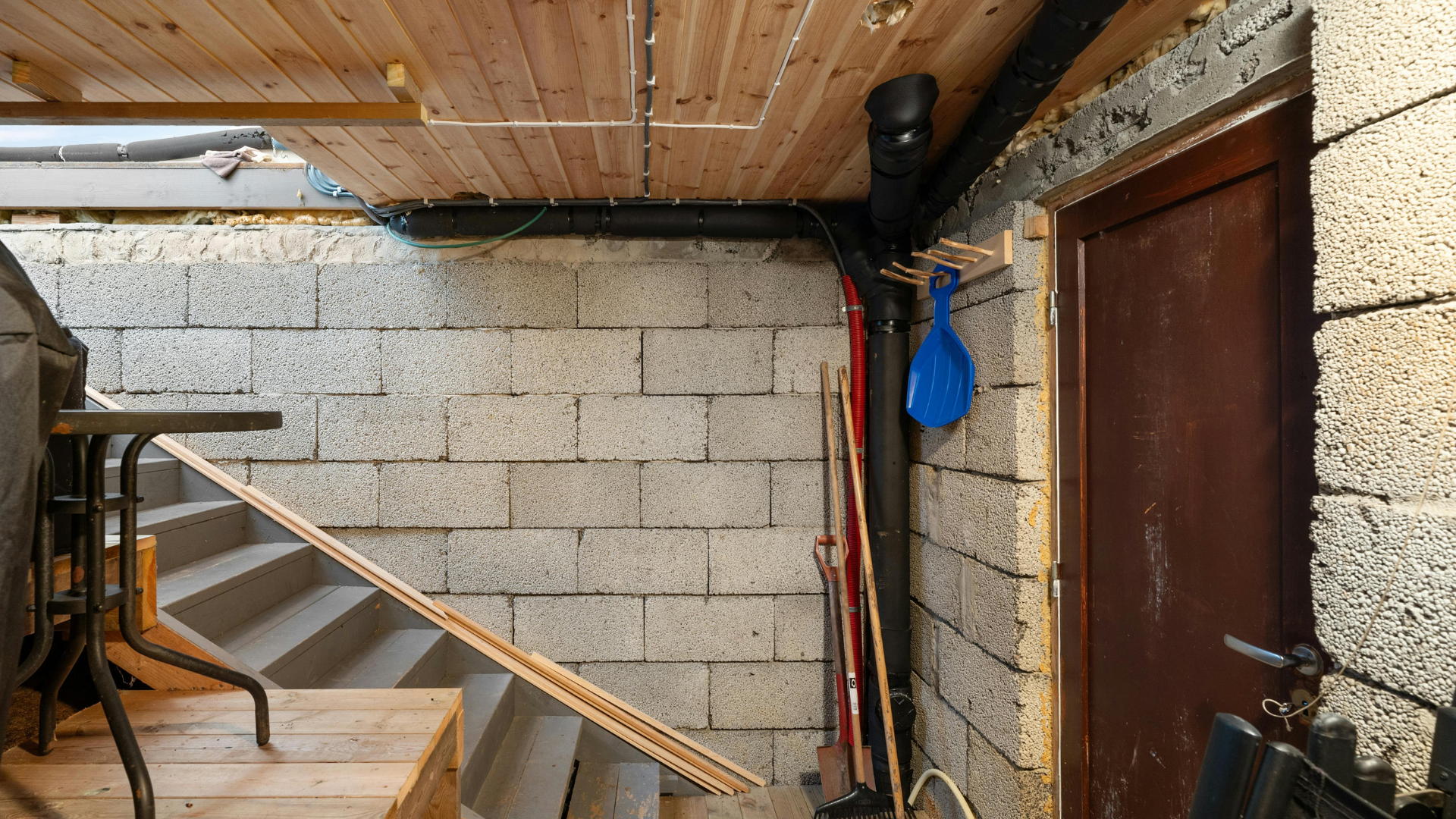 A basement with stairs , a table and a shovel hanging on the wall.