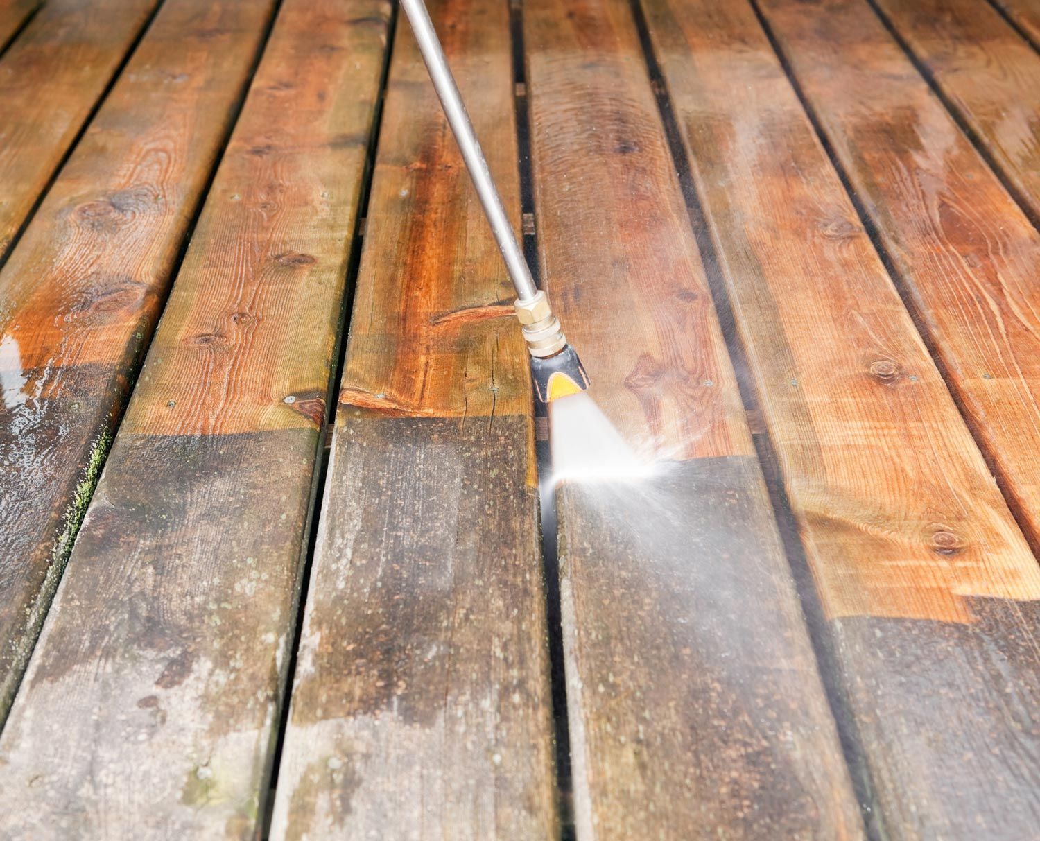 A person is cleaning a wooden deck with a high pressure washer.