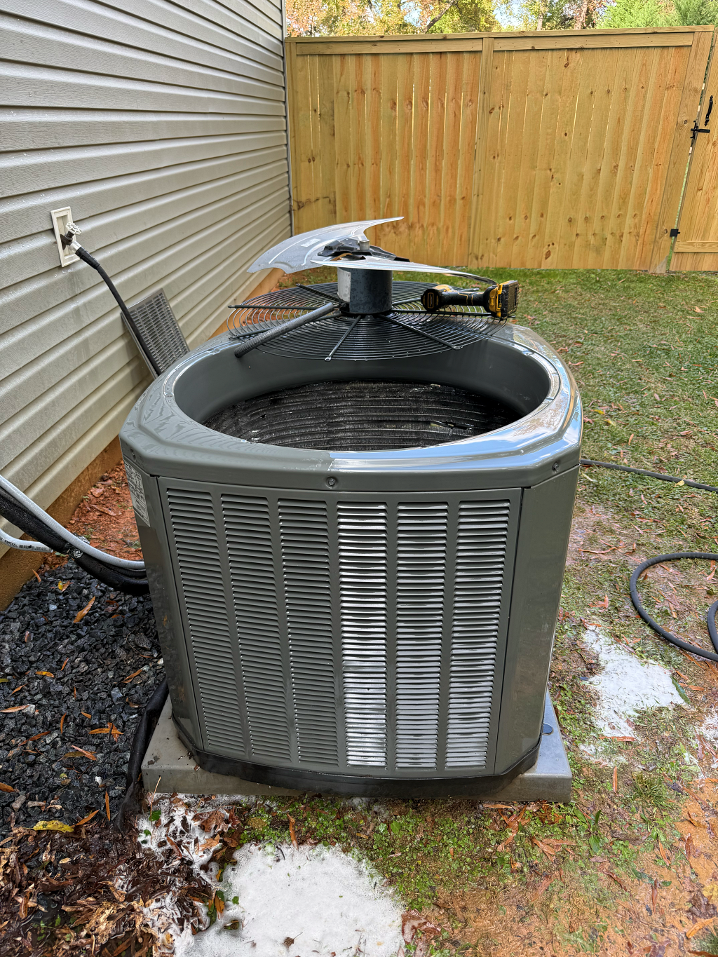 HVAC unit outside a home. Gray metal with a fan on top. Wooden fence and siding visible.
