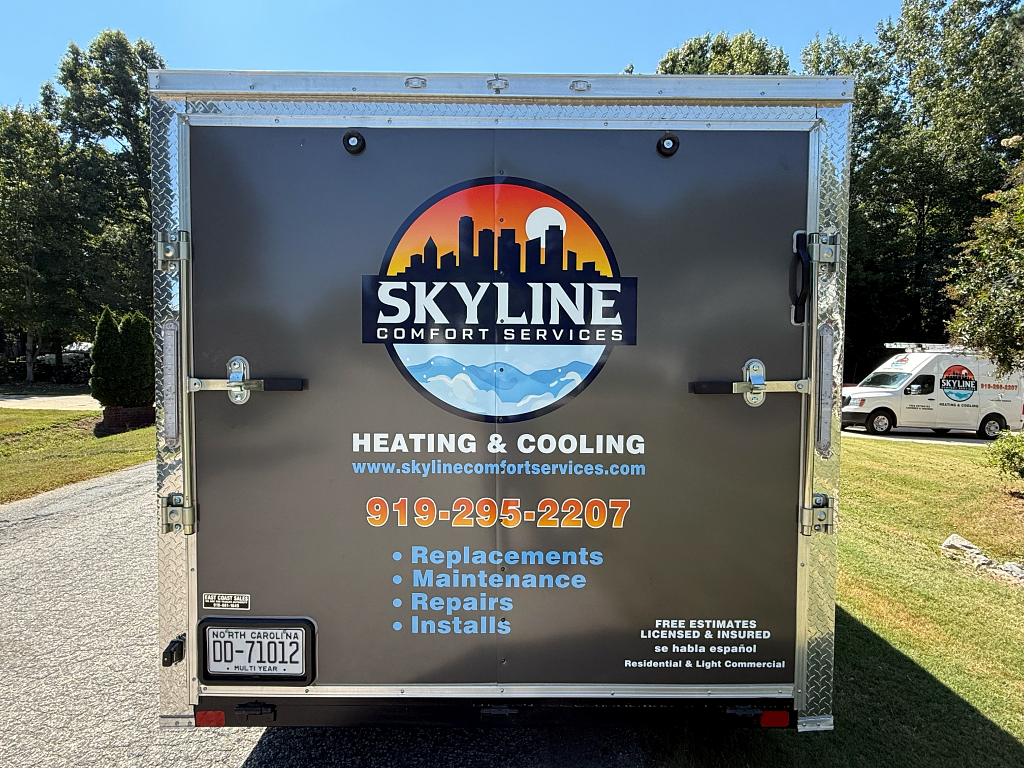 Rear view of a trailer for Skyline Comfort Services with logo and contact information. Another service van is visible.