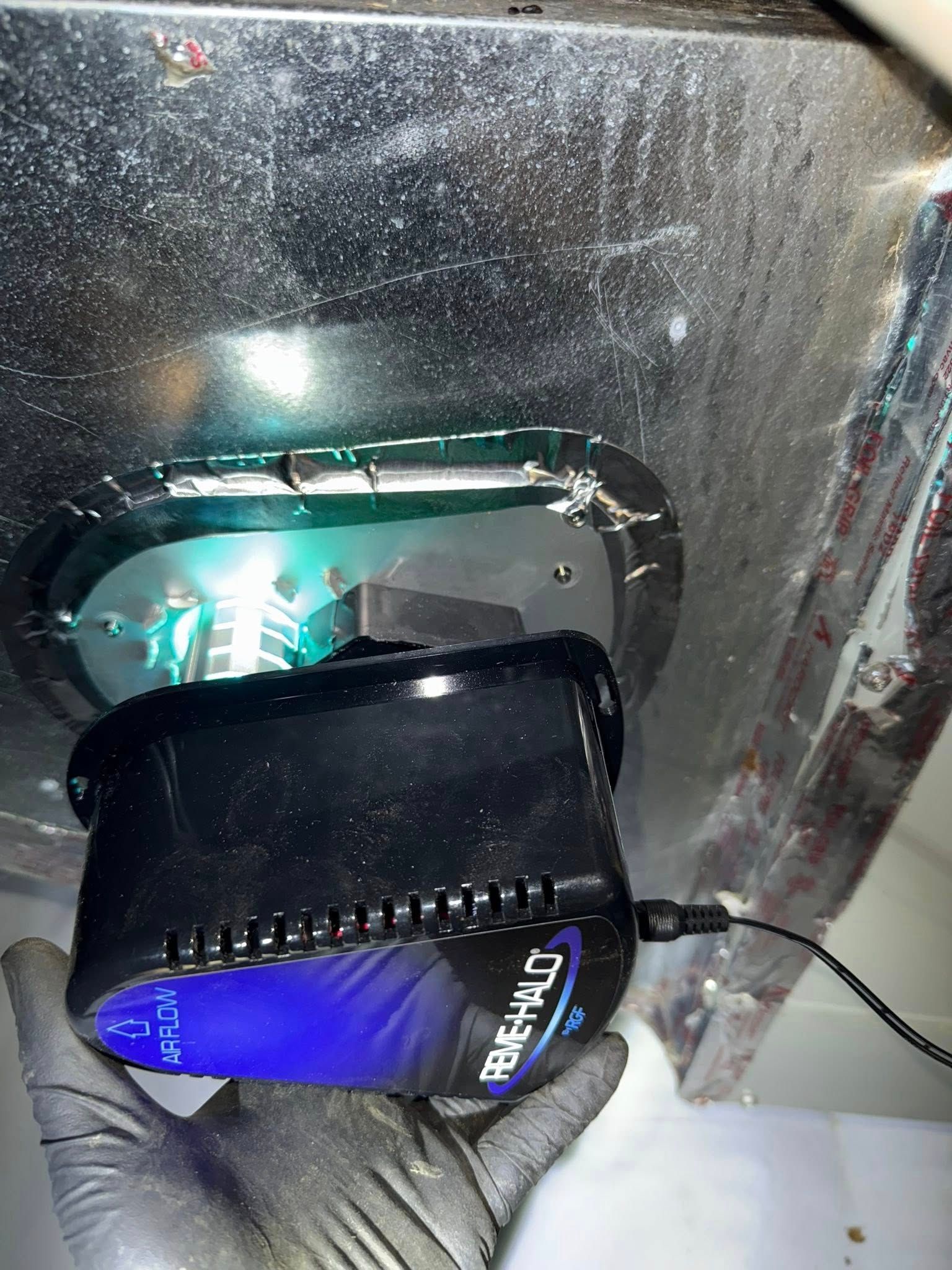 Skyline Comfort Services LLC - air purifier unit, installed inside a metal duct, emitting a green glow.