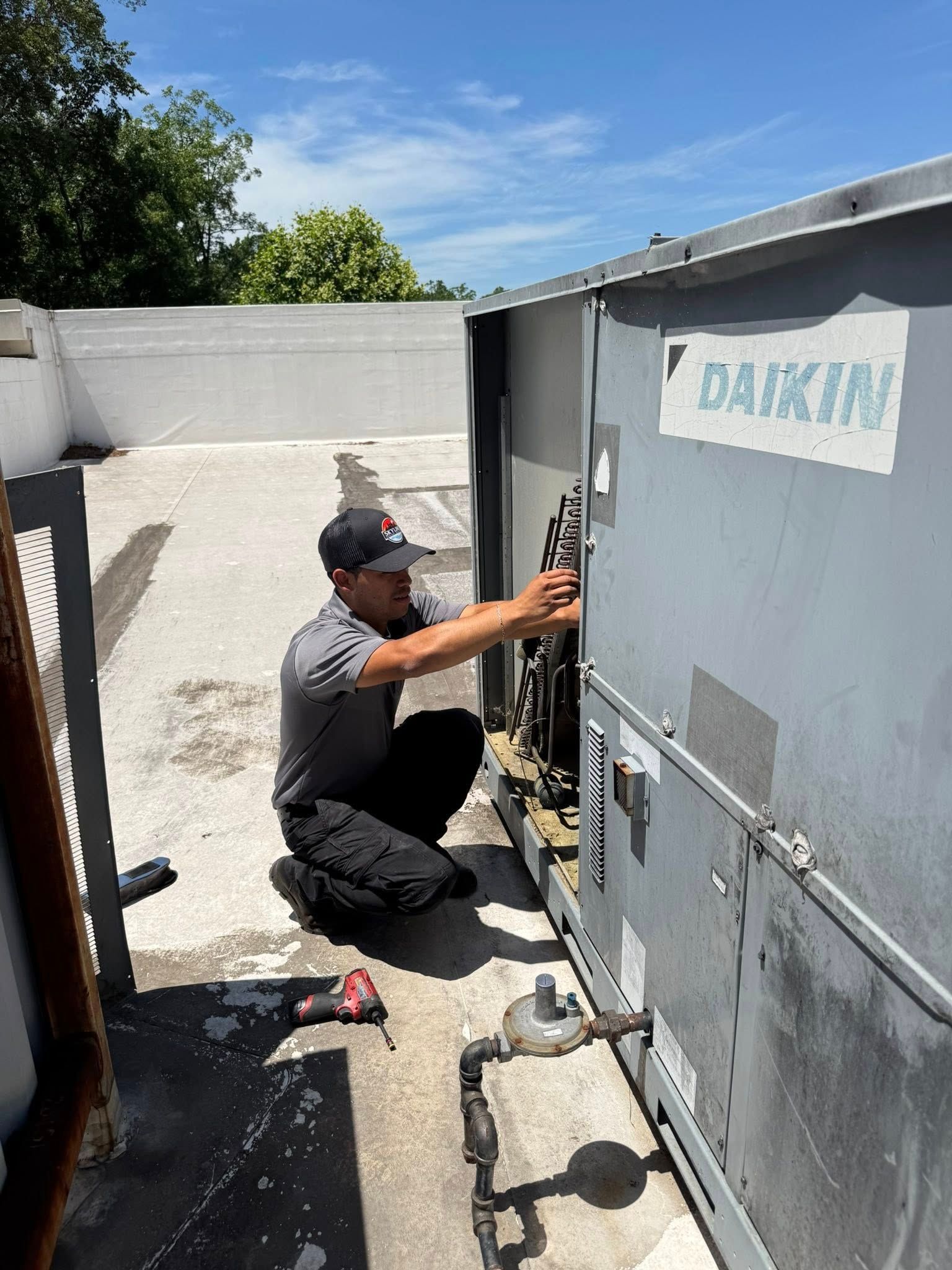 Skyline Comfort Services LLC - HVAC technician kneeling, repairing a Daikin unit on a rooftop, blue sky.