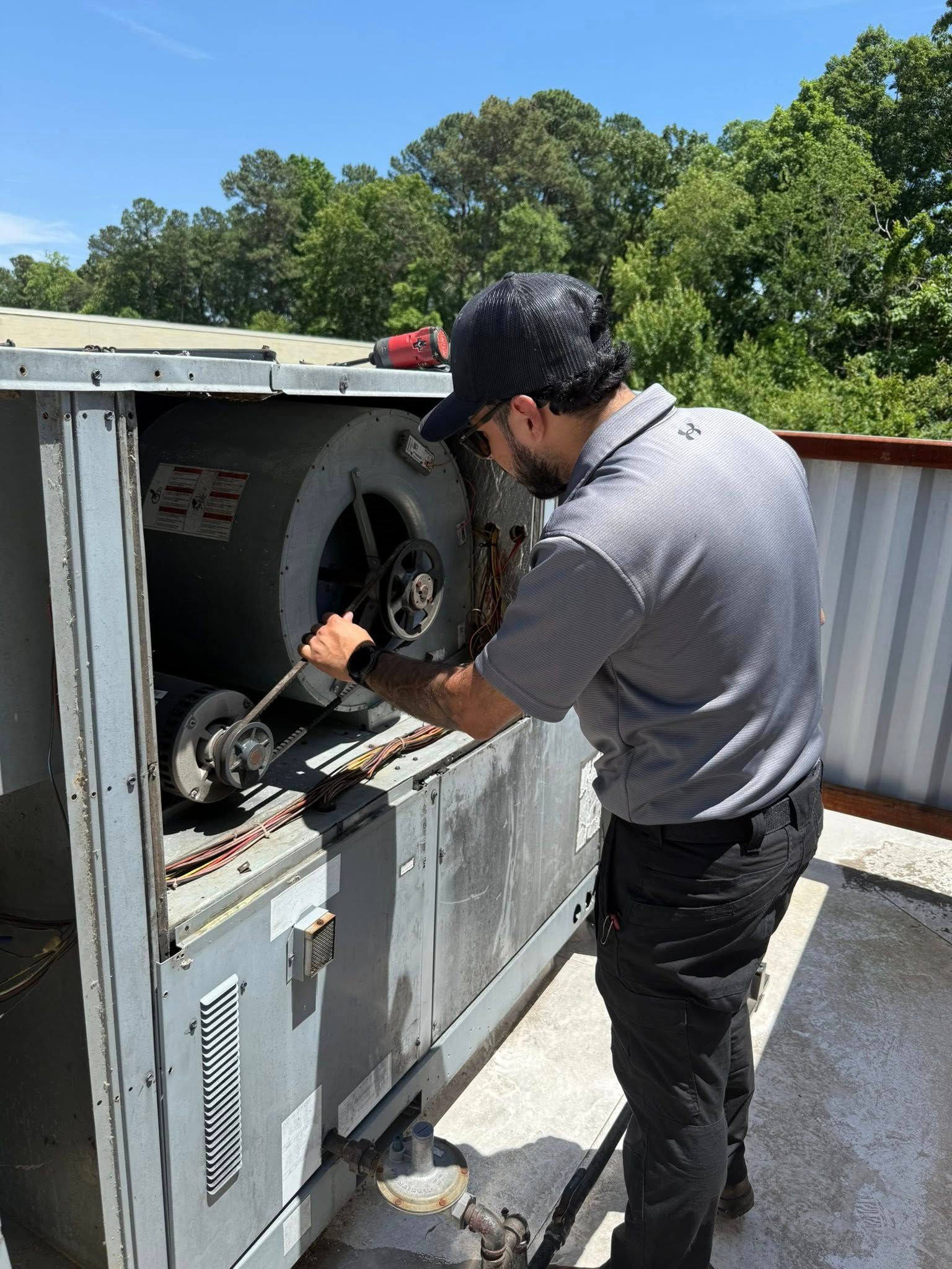Skyline Comfort Services LLC - Man in gray shirt repairing HVAC unit on a rooftop, sunny day.
