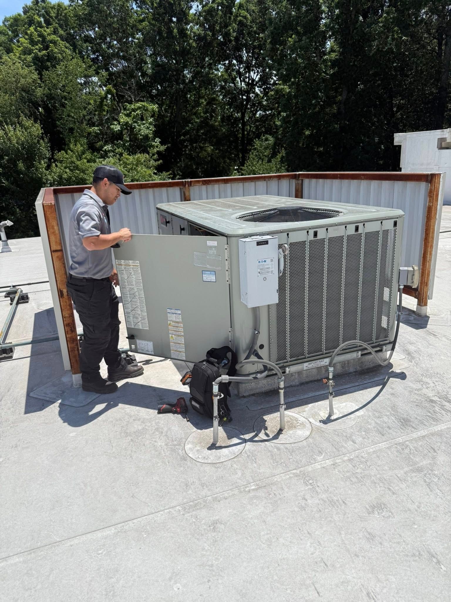Skyline Comfort Services LLC - A technician opens the side panel of an outdoor air conditioner on a rooftop.