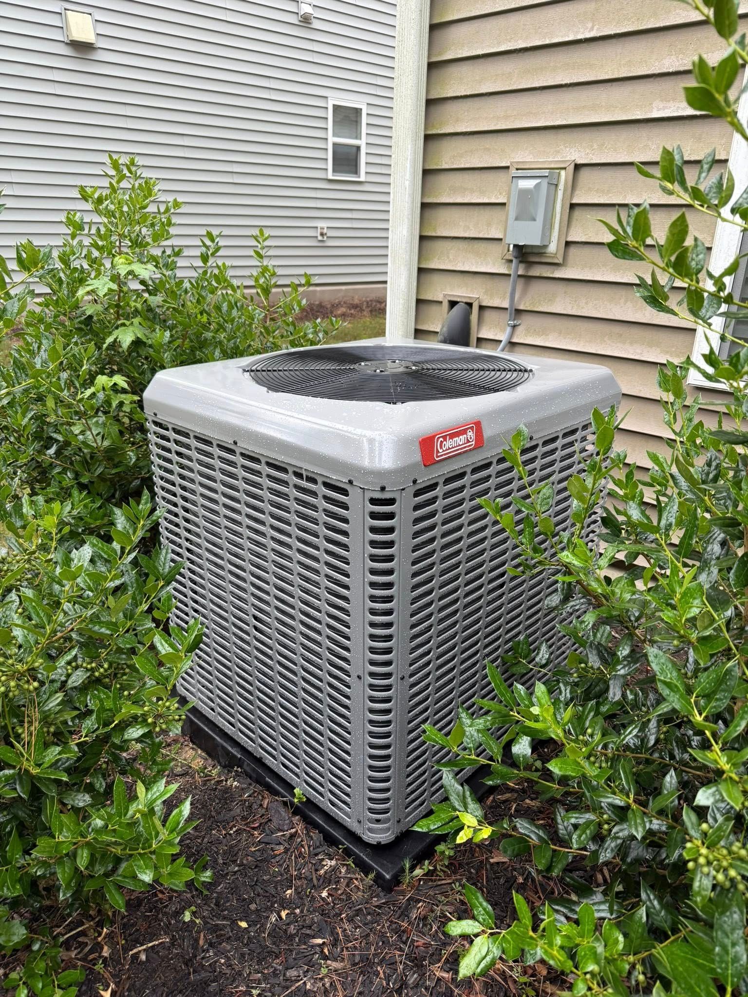 Skyline Comfort Services LLC - Air conditioning unit surrounded by green bushes, mounted on a pad, next to a house.
