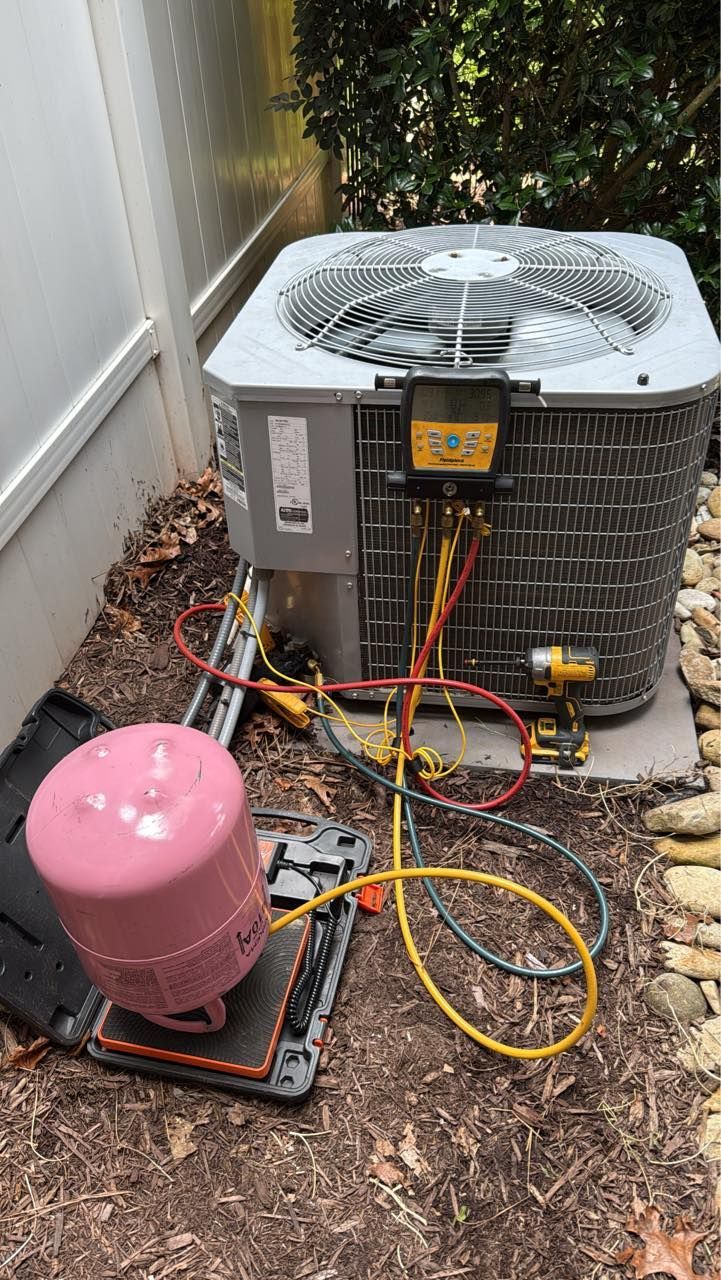 Skyline Comfort Services LLC - An air conditioning unit being serviced outdoors with pink tank connected by colored hoses.