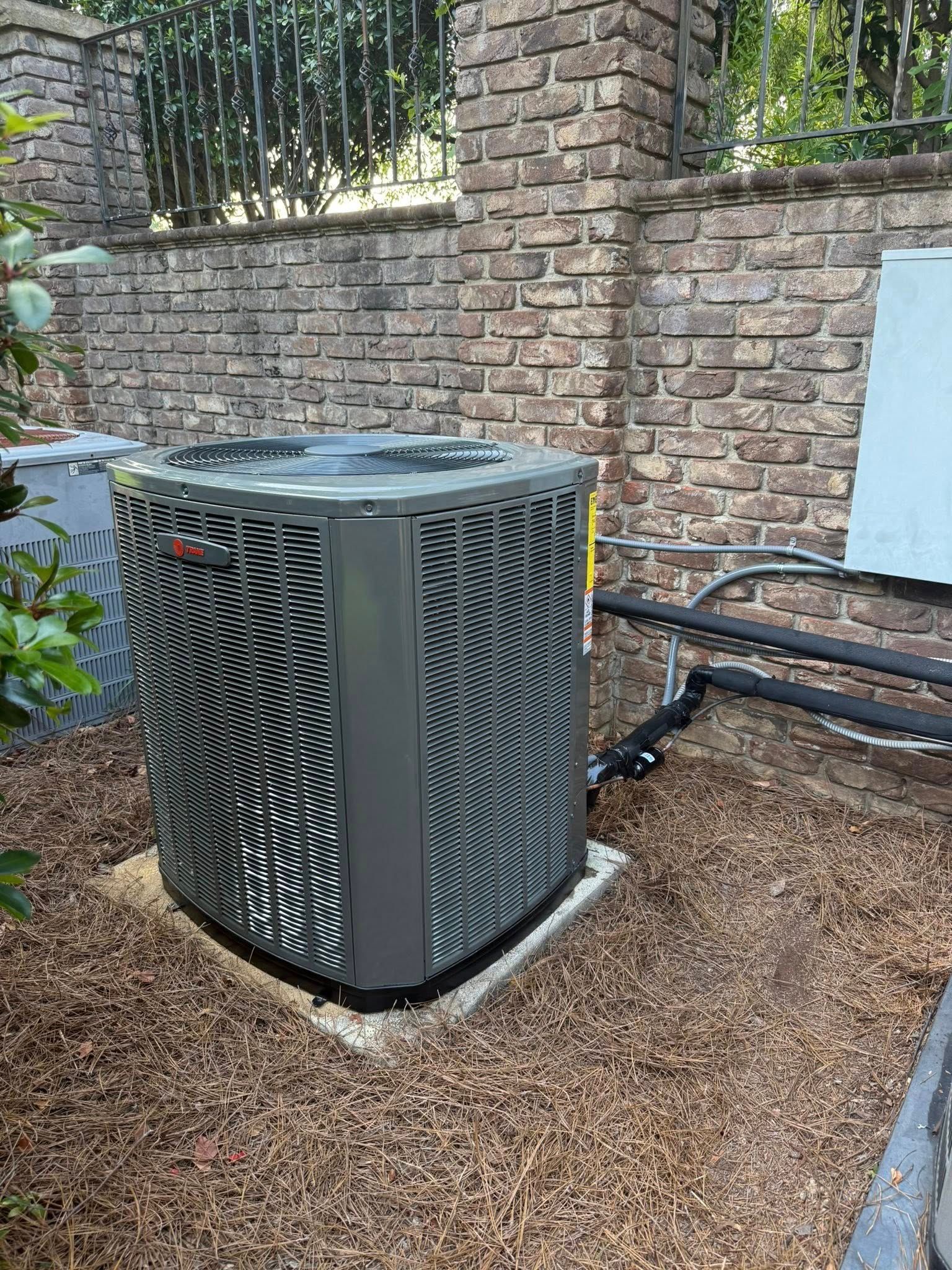 Skyline Comfort Services LLC - An air conditioning unit sits on a concrete pad next to a brick wall and a fence.