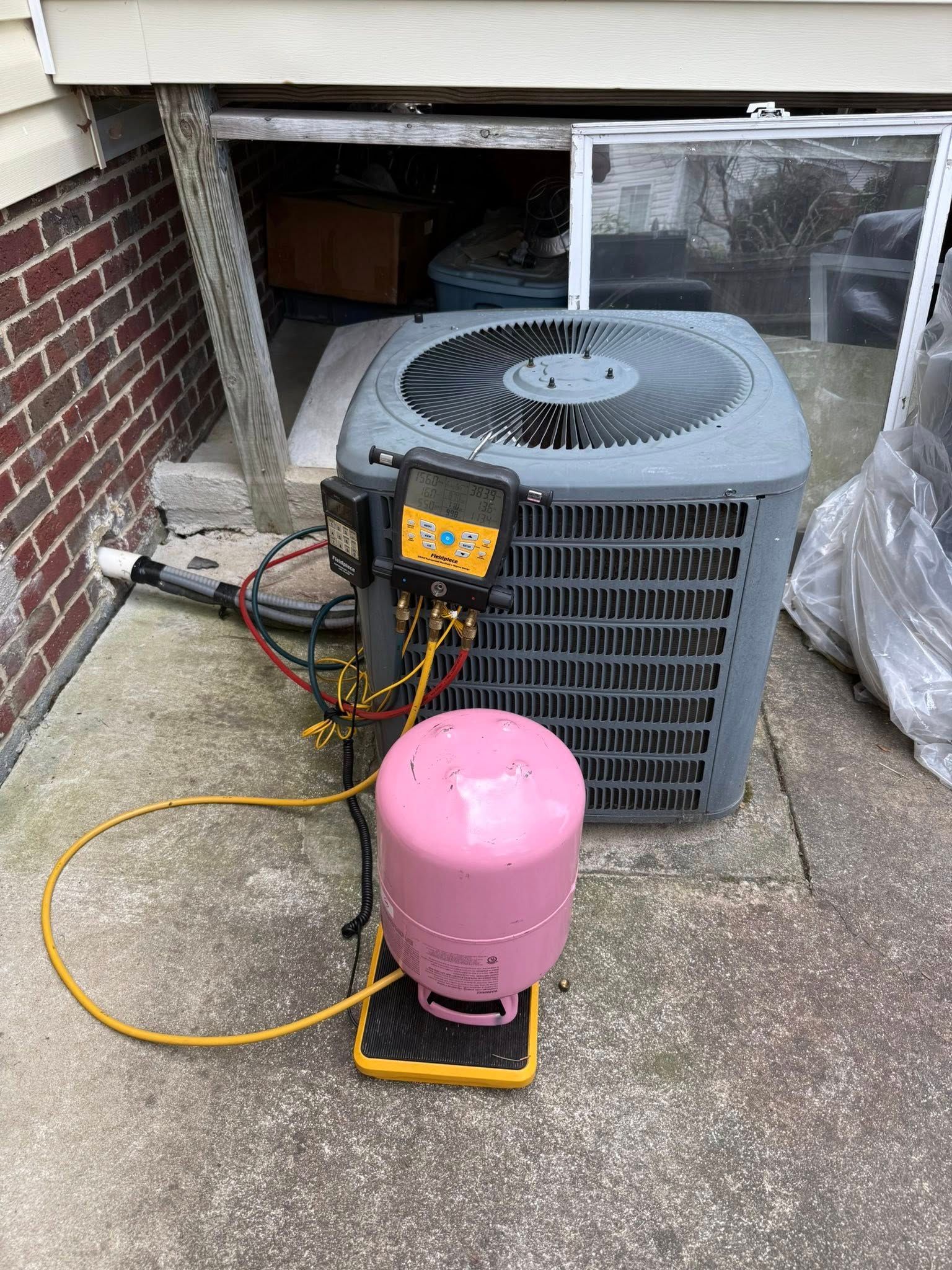 Skyline Comfort Services LLC - AC unit being serviced, pink refrigerant tank on a scale, yellow hoses attached.