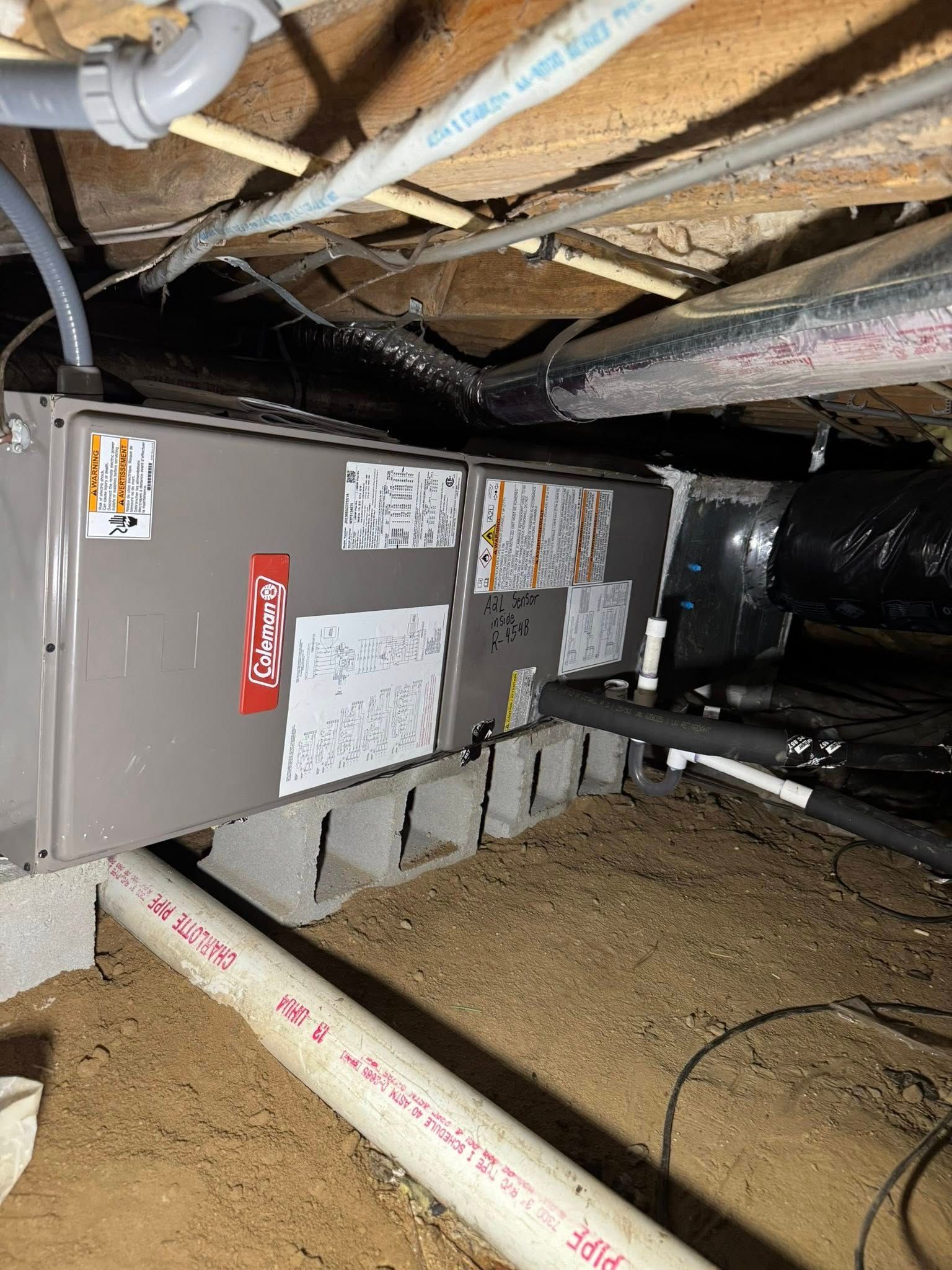 Skyline Comfort Services LLC - HVAC unit on cinder blocks in a crawl space with pipes and ductwork overhead.