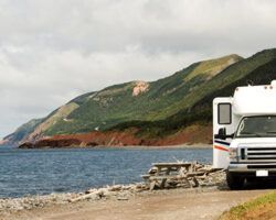 RV parked on a rocky beach with mountains in the background and a picnic table nearby.