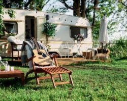 Camper trailer set up outdoors with chair, guitar, table, and umbrella.