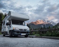 White RV parked on asphalt with mountain view, cloudy sky.