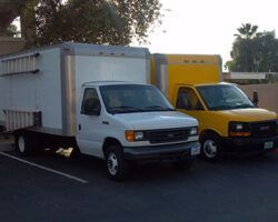 Two box trucks parked outdoors: one white, one yellow.