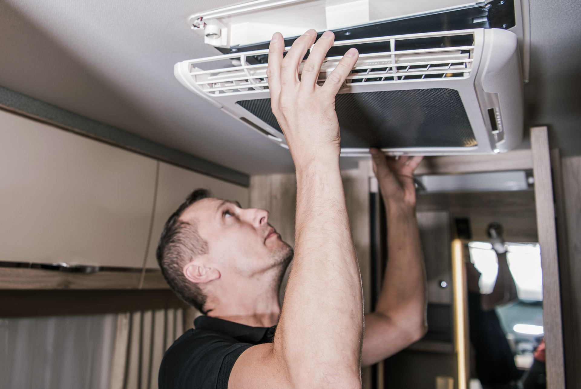 Man removing air vent cover in a vehicle, looking up, indoors.