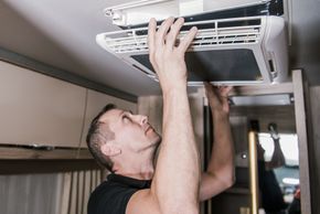 Man removing air vent cover in a vehicle, looking up, indoors.