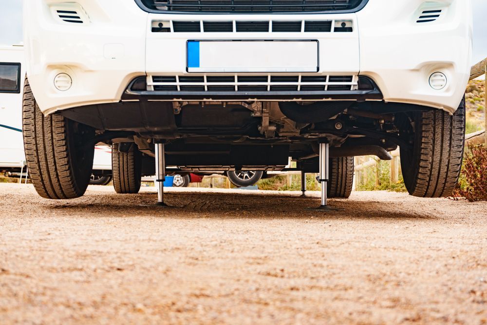 White RV with leveling jacks on a sandy surface.