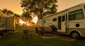 RVs parked in a grassy campsite at sunset, with chairs and table set up.