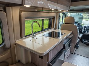 RV kitchen with sink, cooktop, and window view of greenery.