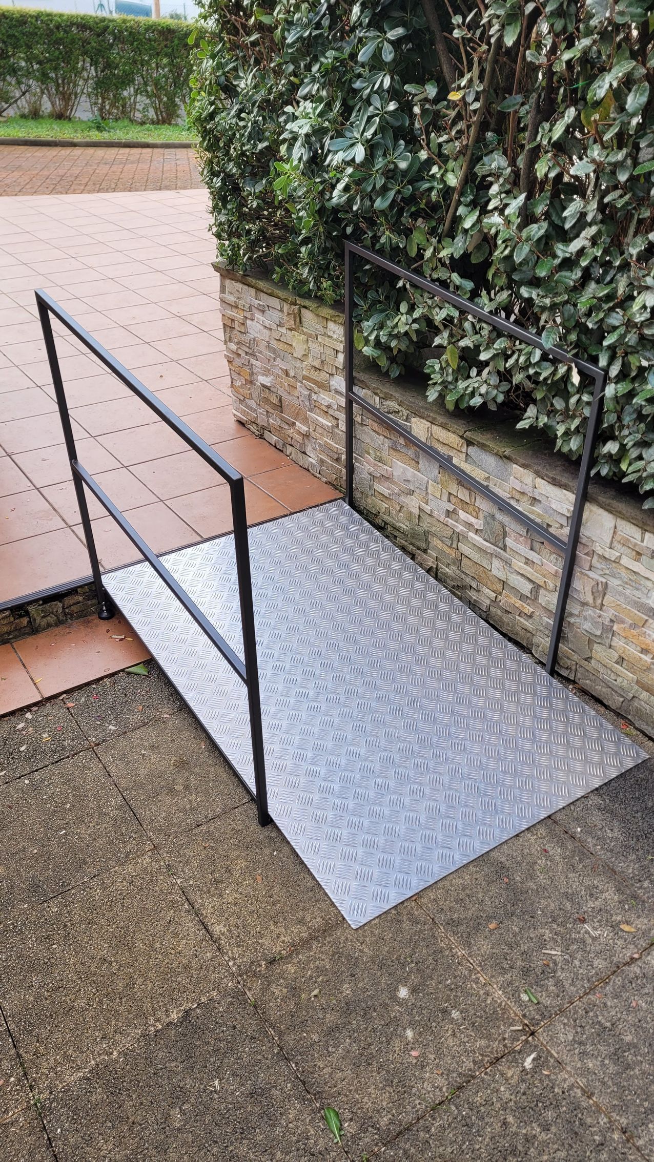 une rampe métallique avec une balustrade repose sur le sol à côté d'une passerelle en brique.