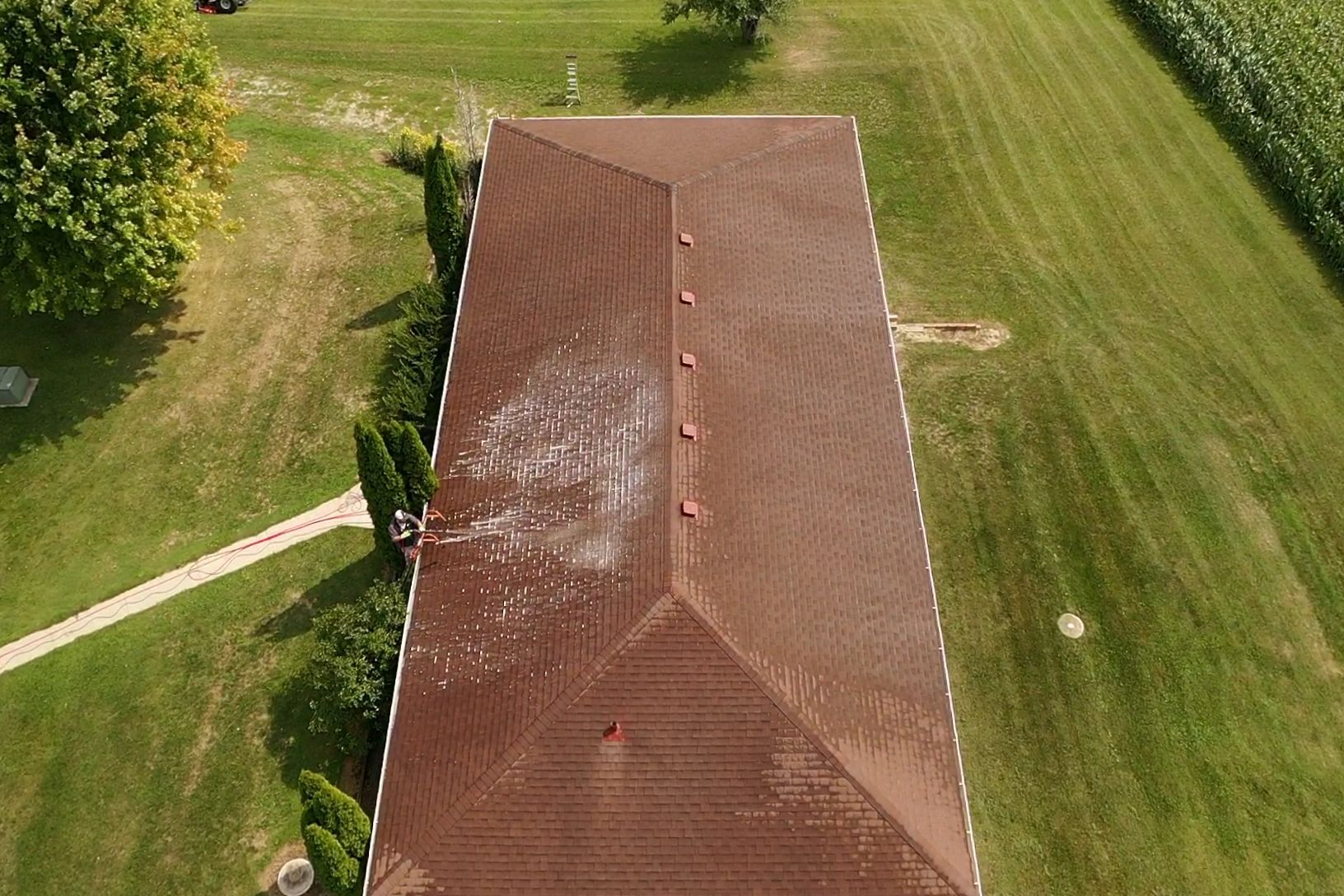 An aerial view of a house with a red roof surrounded by grass and trees.