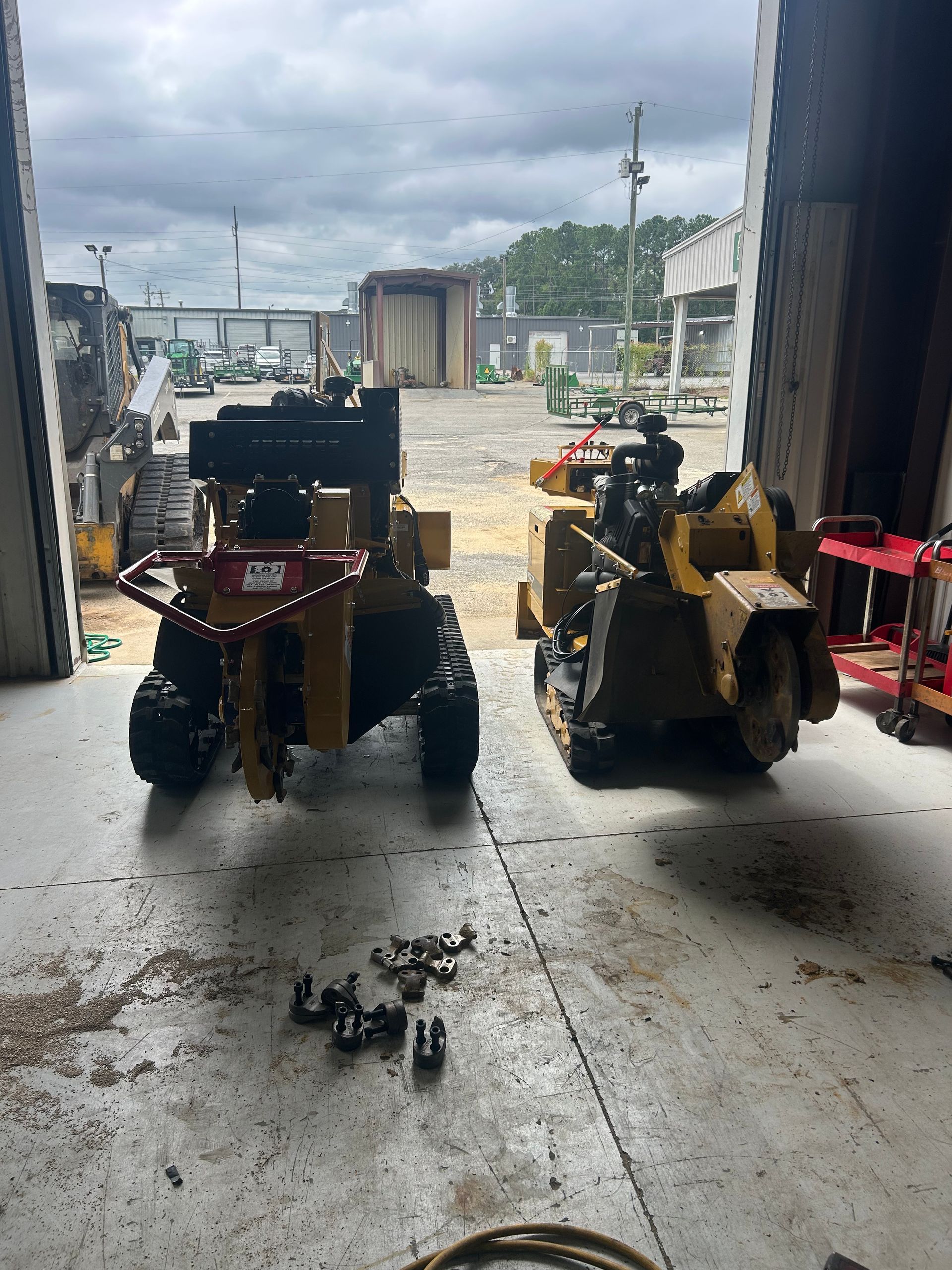 Two yellow stump grinders inside a garage. Cloudy day outside.