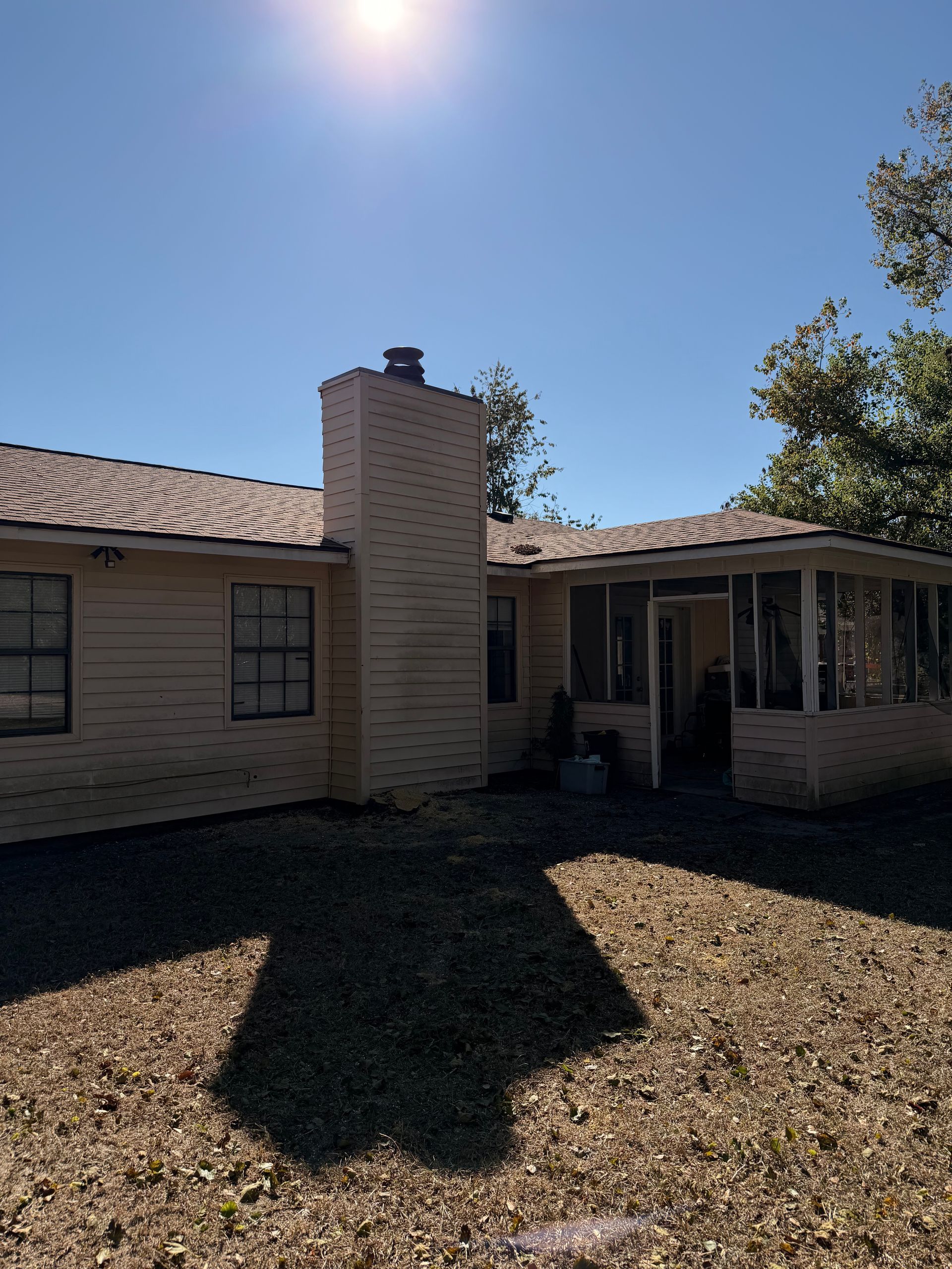 Backyard view of a brick house with a chimney and screened porch under a bright sunny sky.