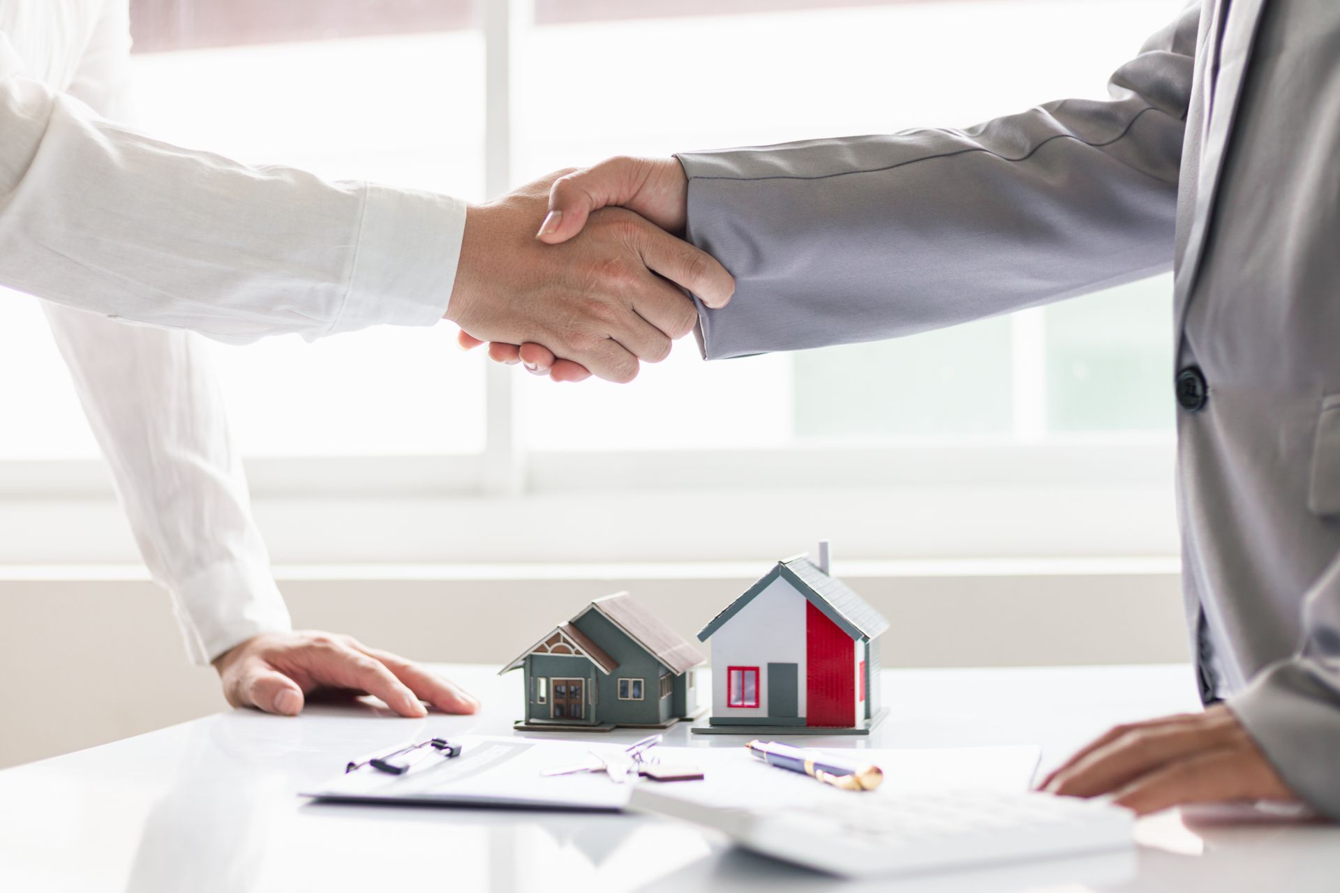 Two people are shaking hands over a table with small houses on it.