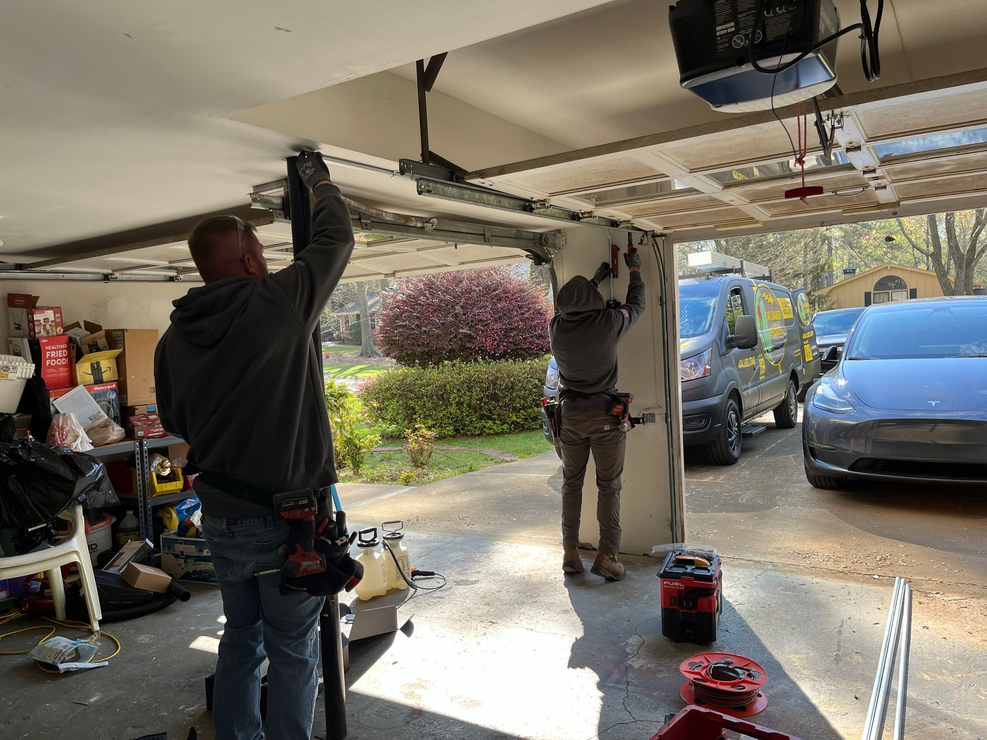 Two men are working on a garage door in a garage.