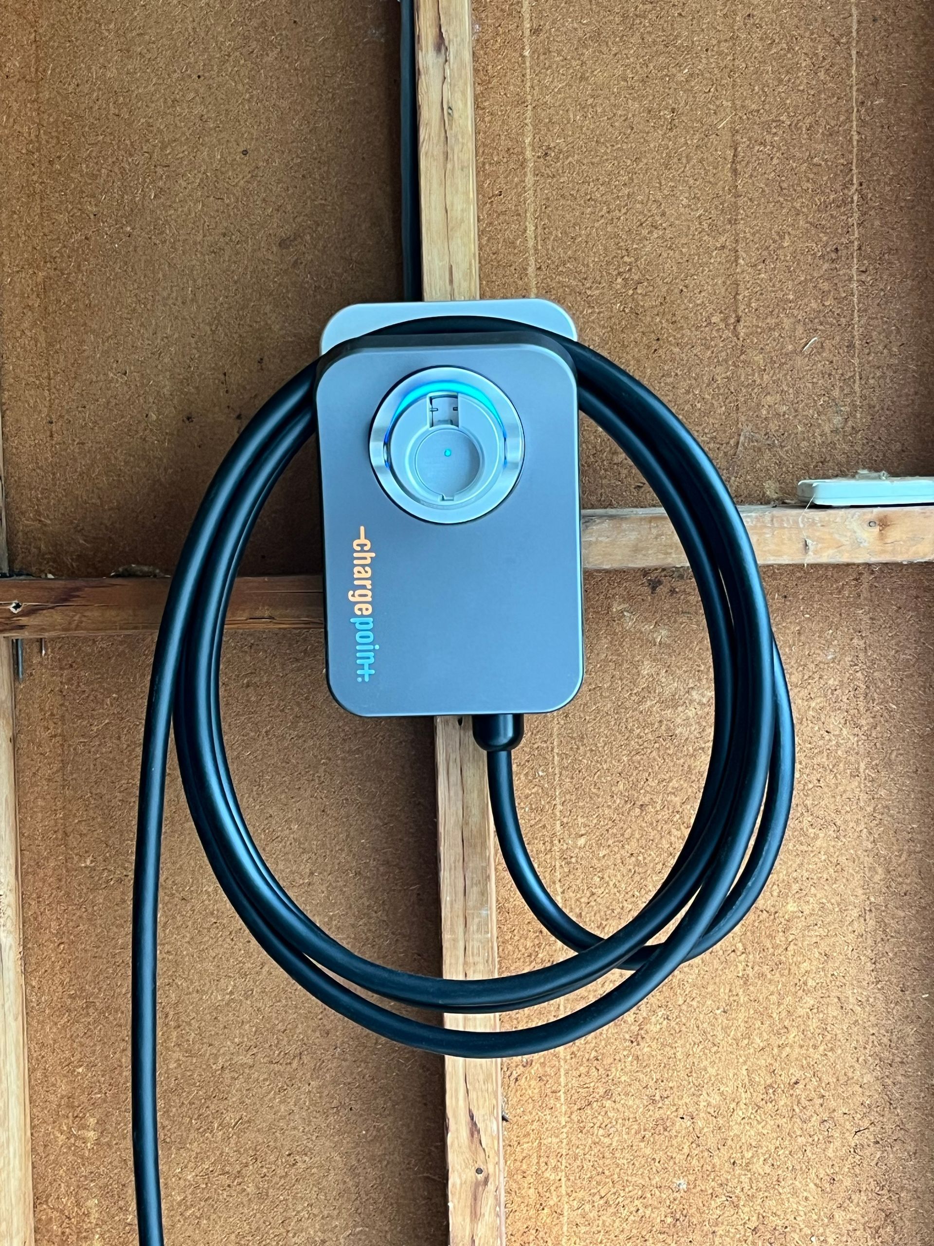 A gray box with a cord attached to it is hanging on a wooden wall.