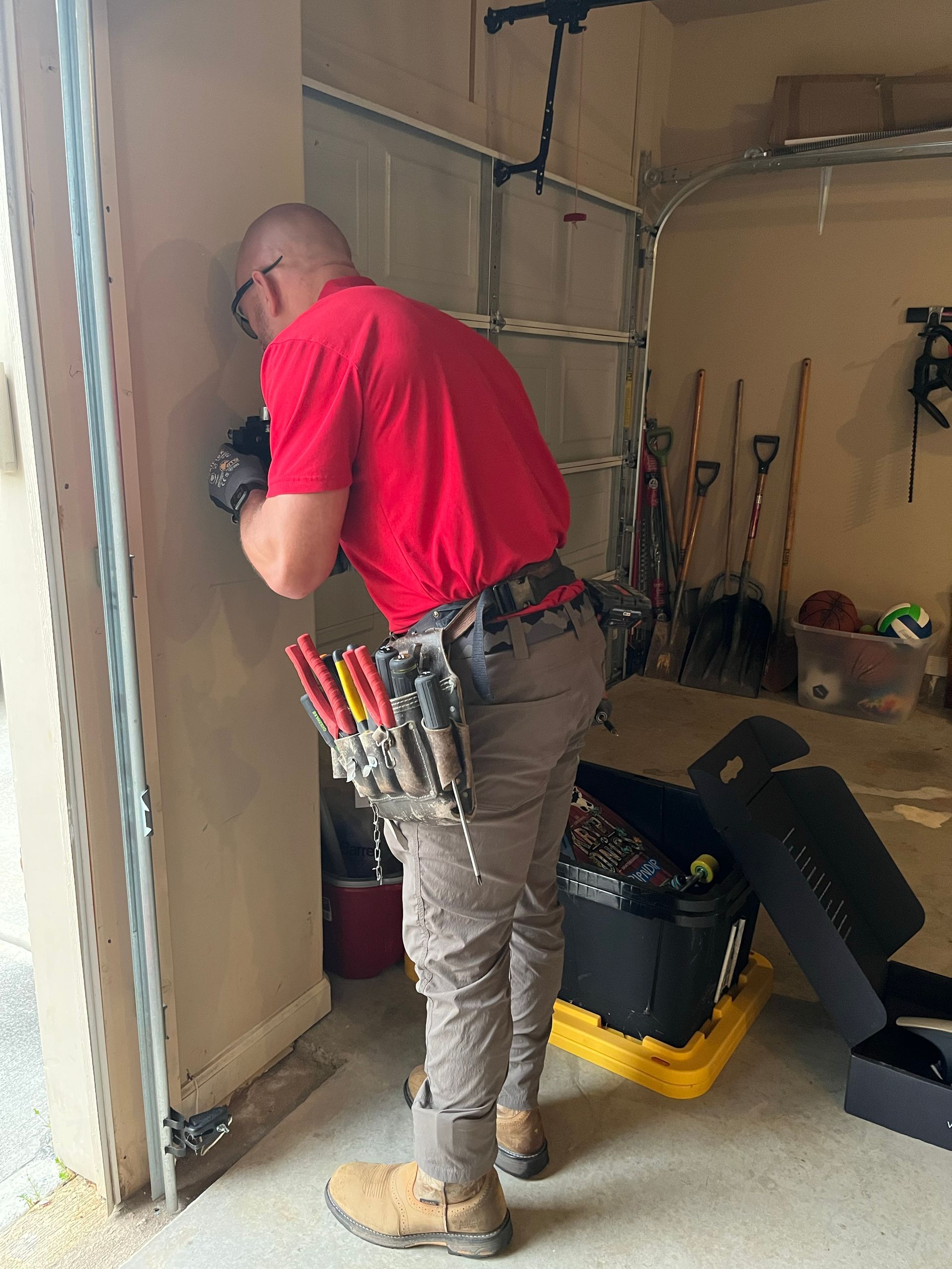 A man in a red shirt is working on a garage door.