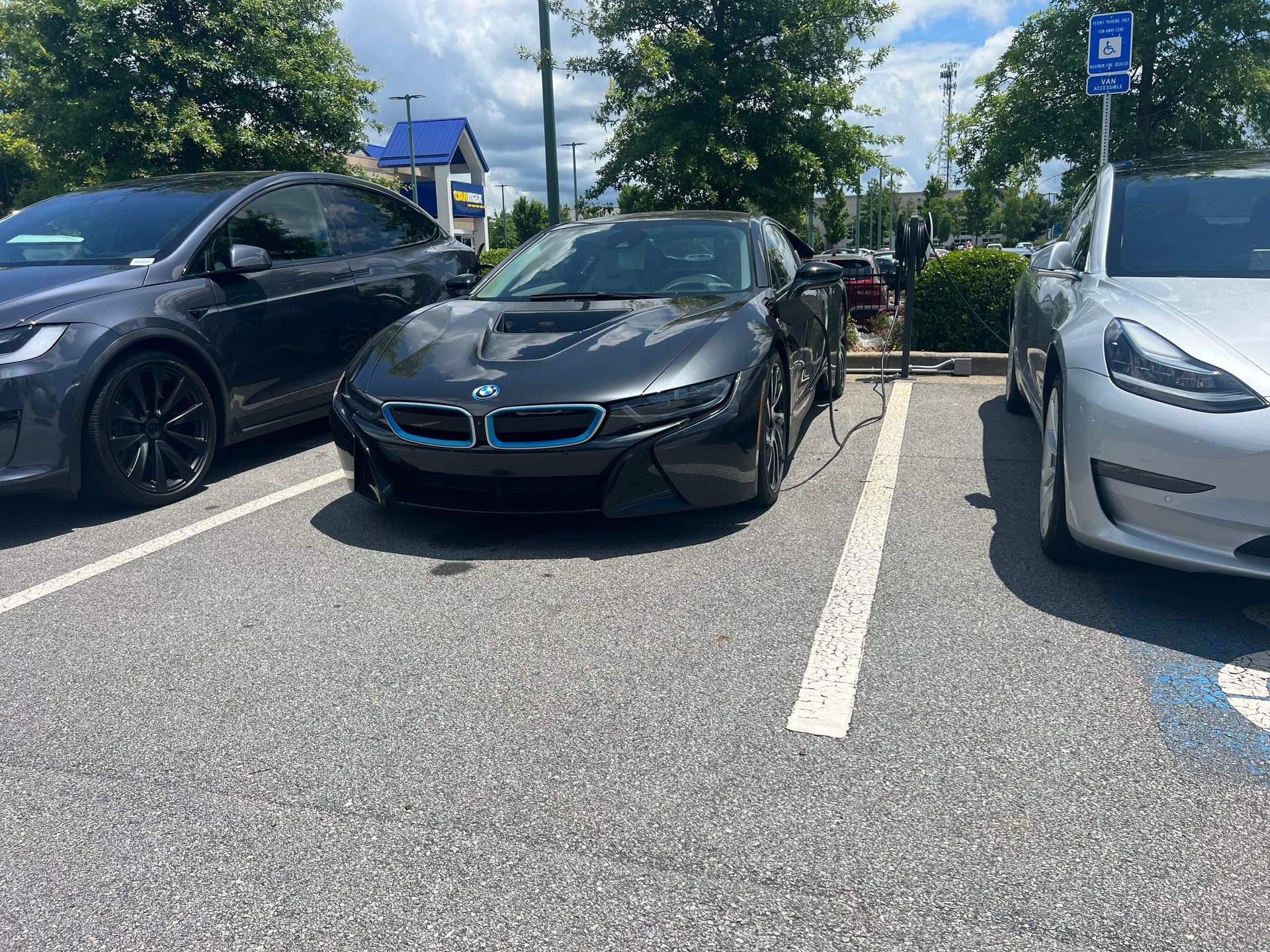 A bmw i8 is charging in a parking lot next to a tesla model 3.