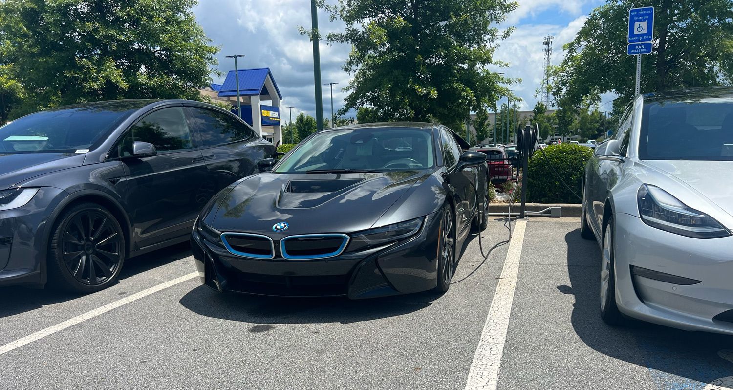 A bmw i8 is being charged in a parking lot next to a tesla model 3.