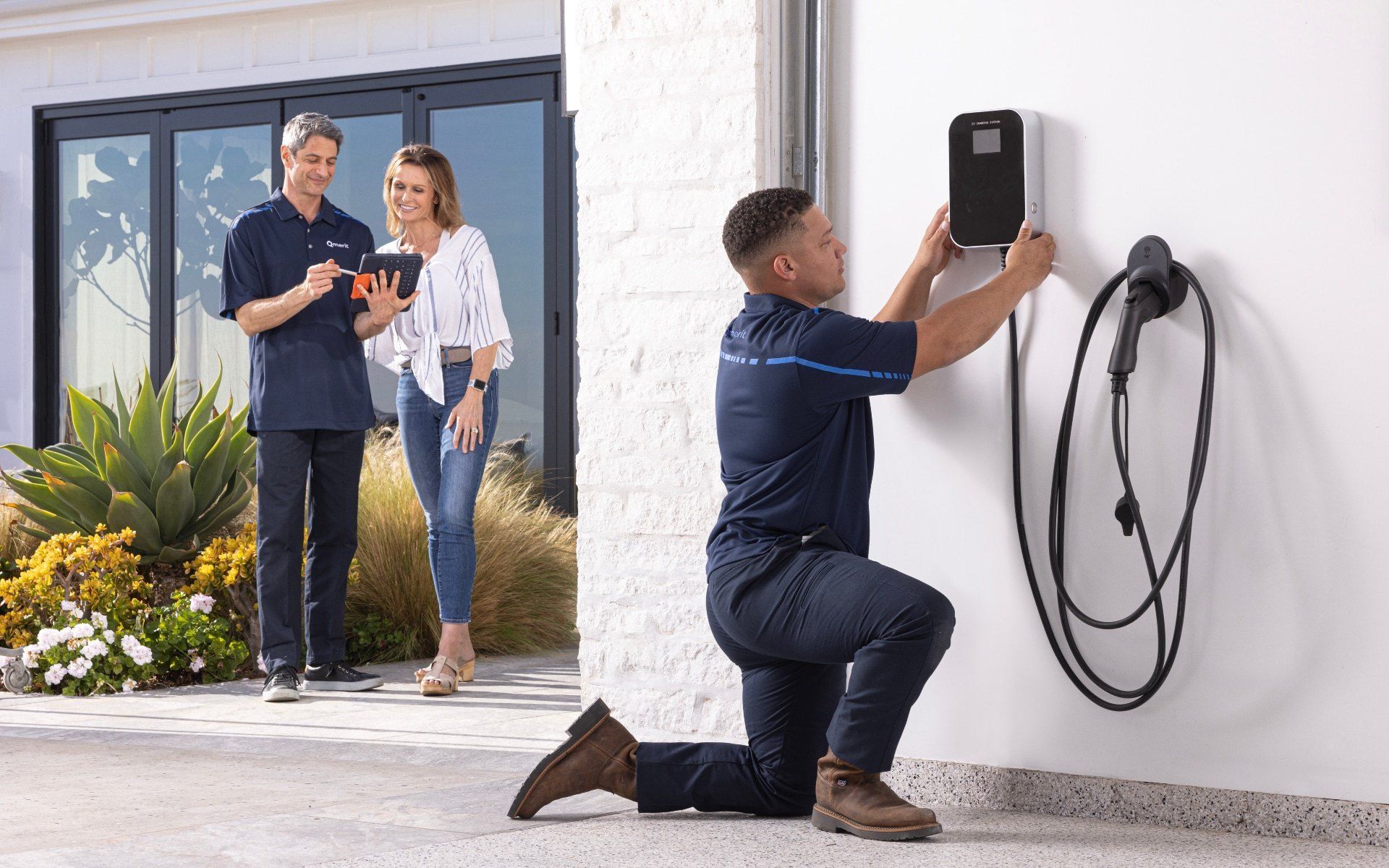 Two men are working on an electrical panel on a wall.