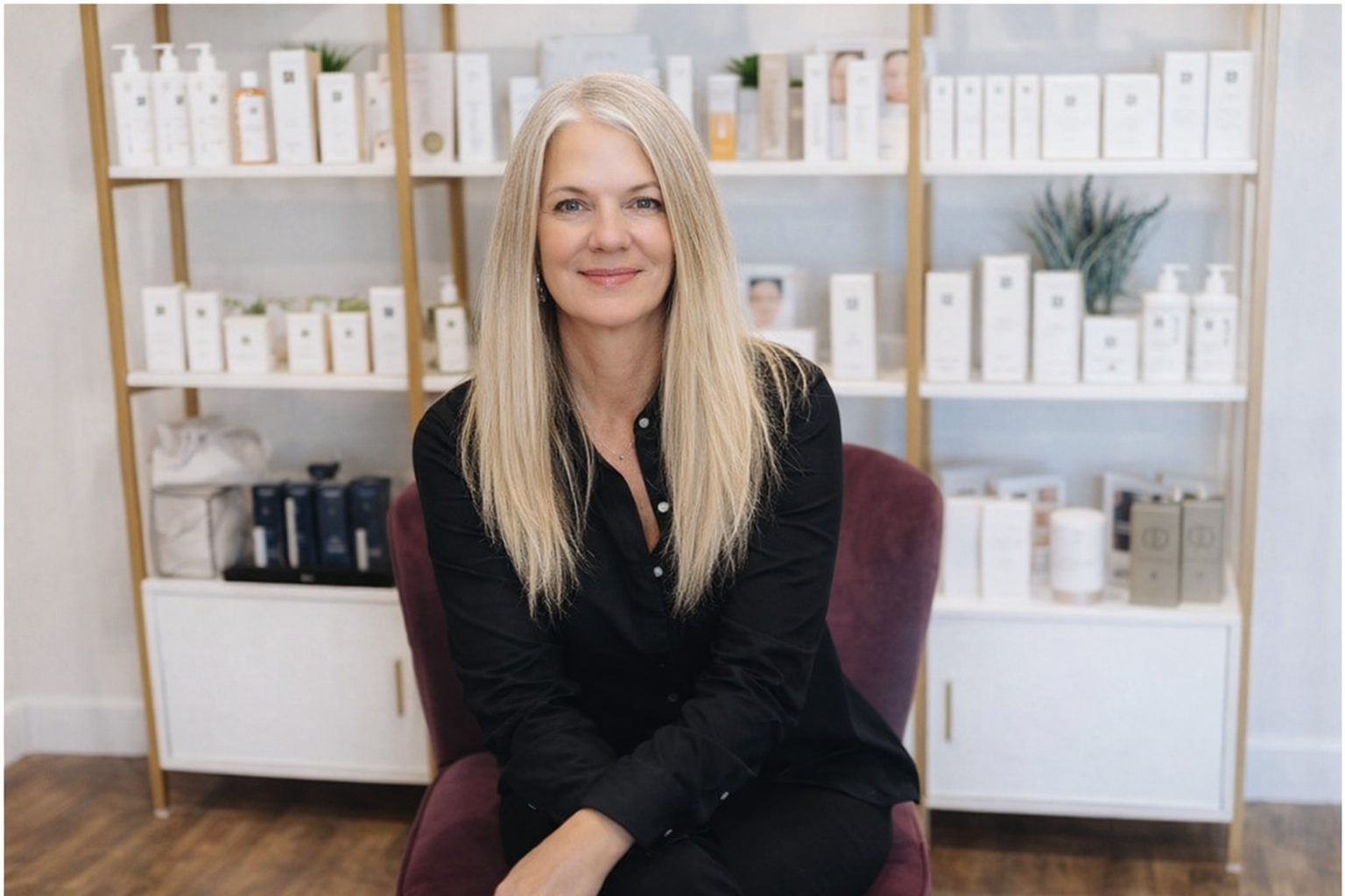 Woman with long gray hair seated in front of shelves of beauty products.