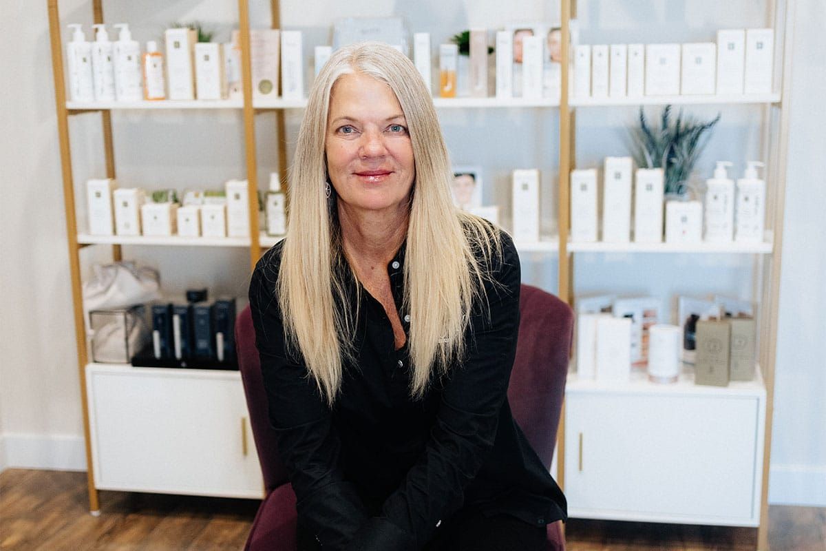 A woman is sitting in a chair in front of a shelf of beauty products.