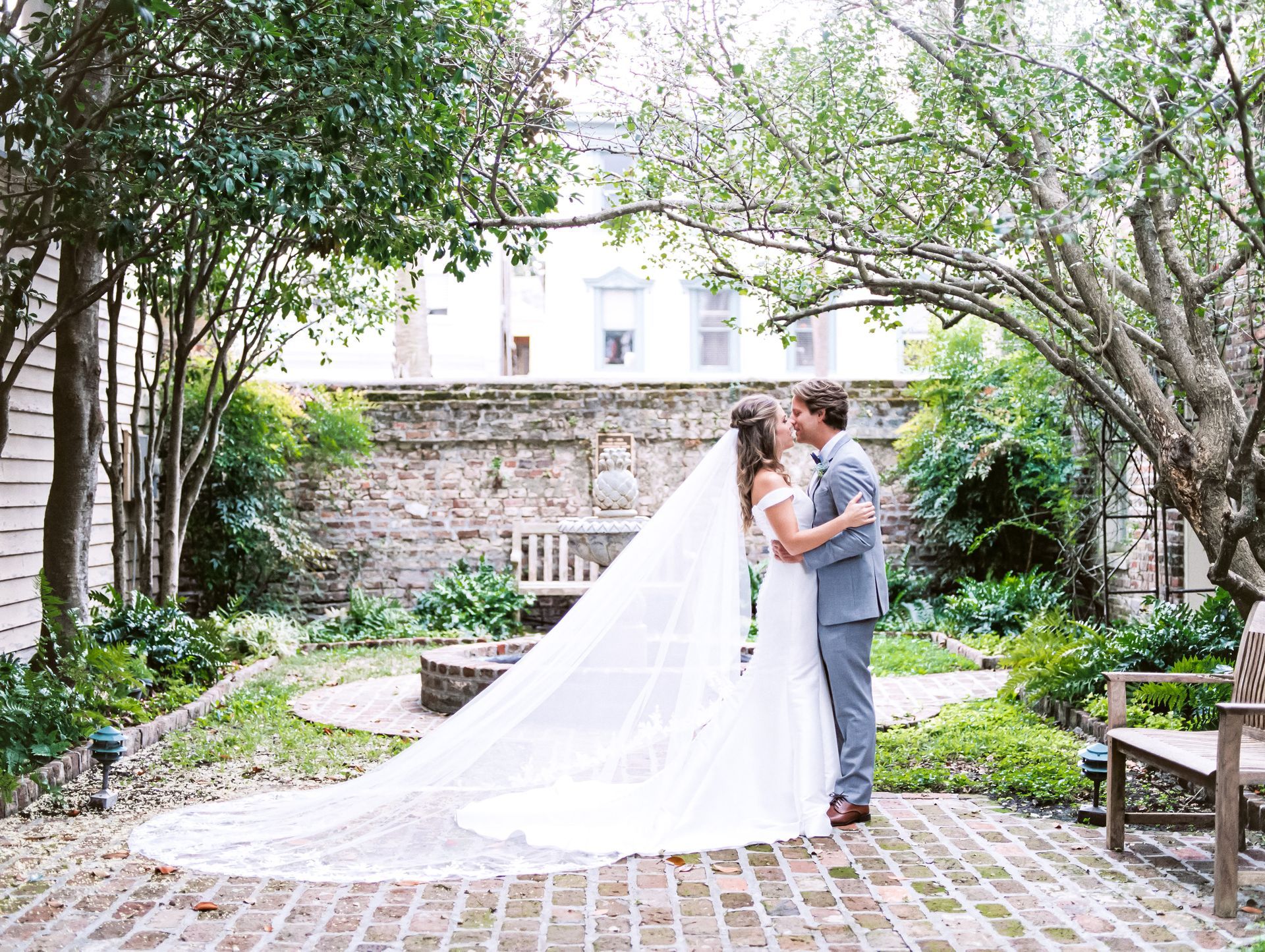 A bride and groom are kissing in a garden . the bride is wearing a long veil.