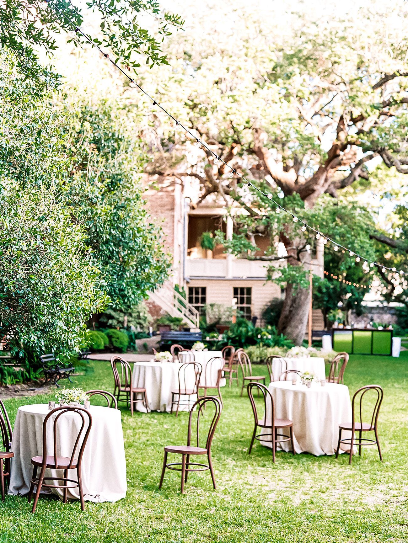 Tables and chairs are set up in the grass in front of a house.