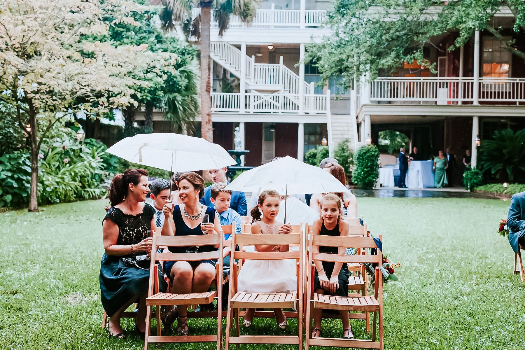 A group of people are sitting in folding chairs holding umbrellas.