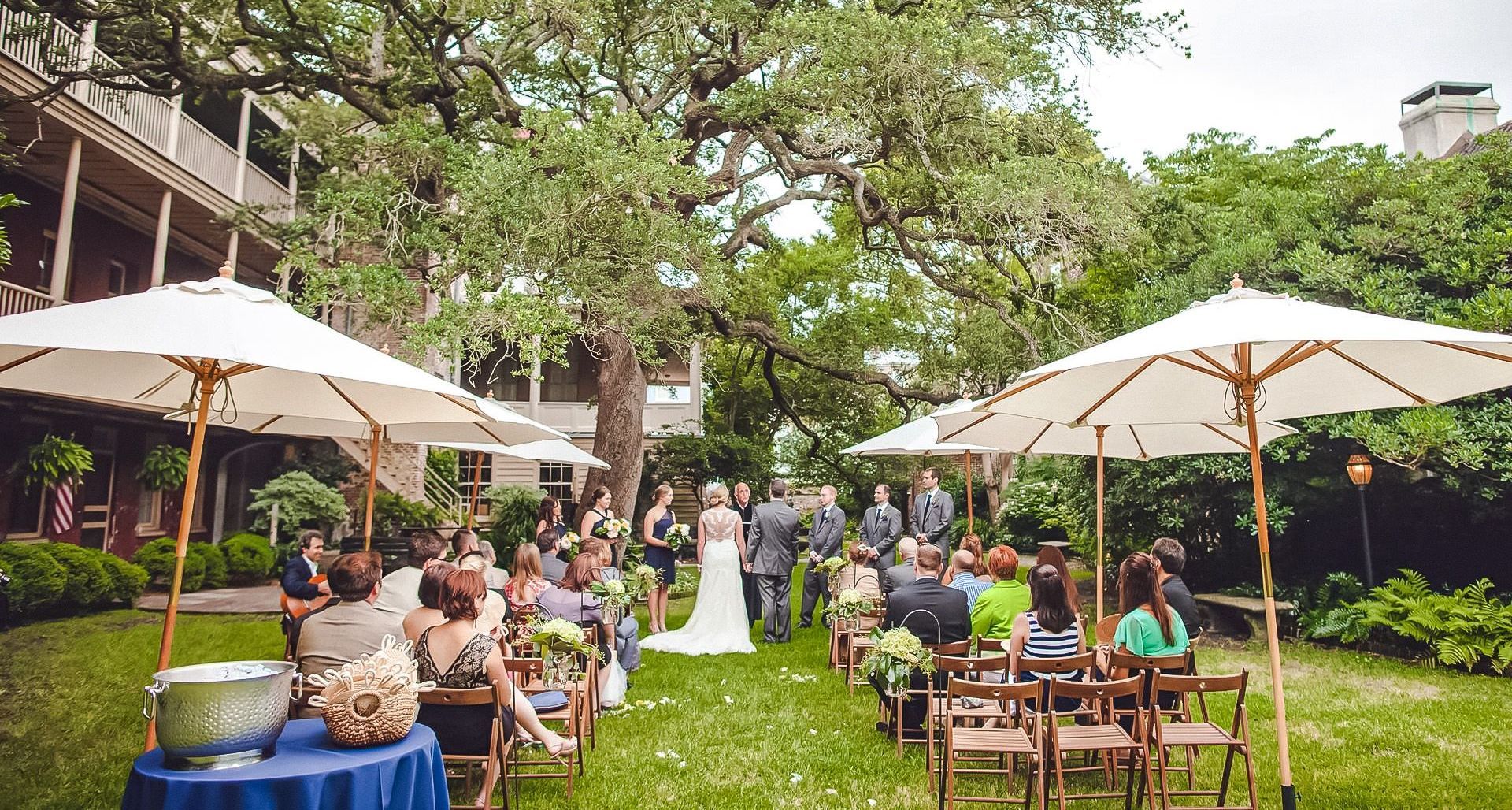 A bride and groom are walking down the aisle at a wedding ceremony under umbrellas.