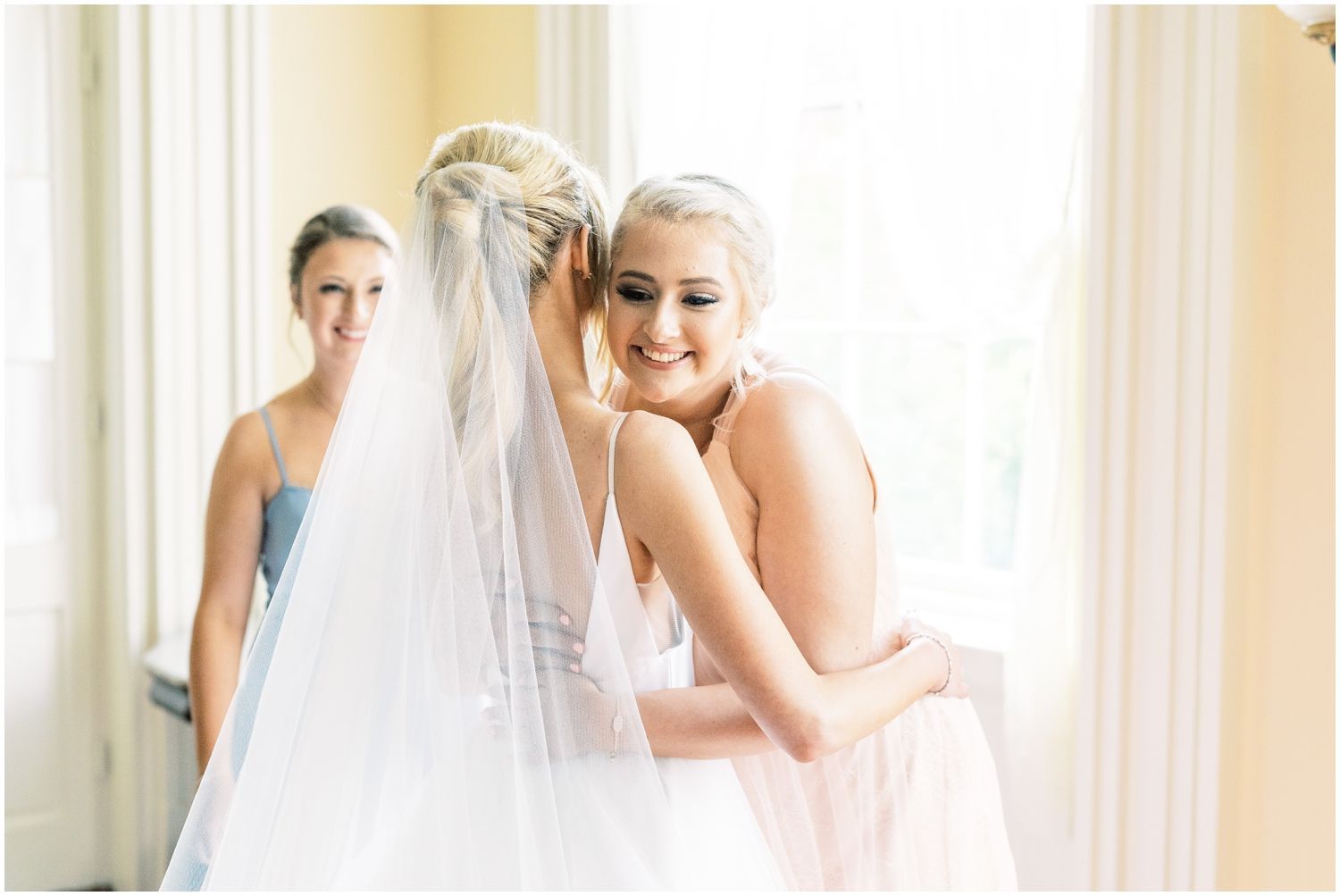 A bride and her bridesmaid are hugging each other in a room.