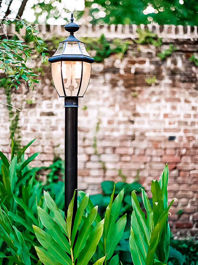 A lamp post in a garden with a brick wall in the background