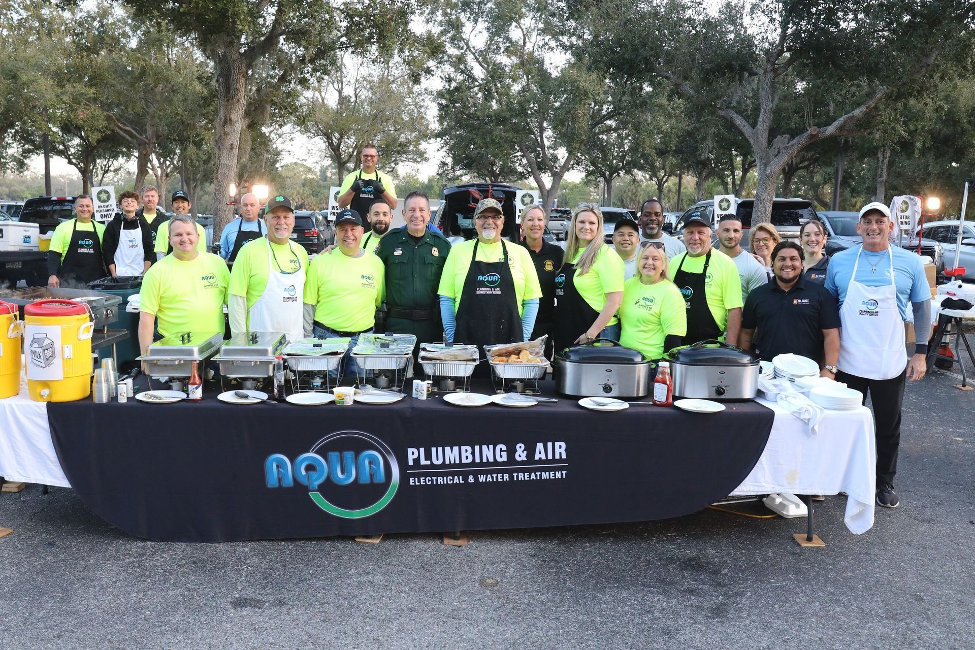 A group of people standing behind a food table with Aqua Plumbing & Air logo.