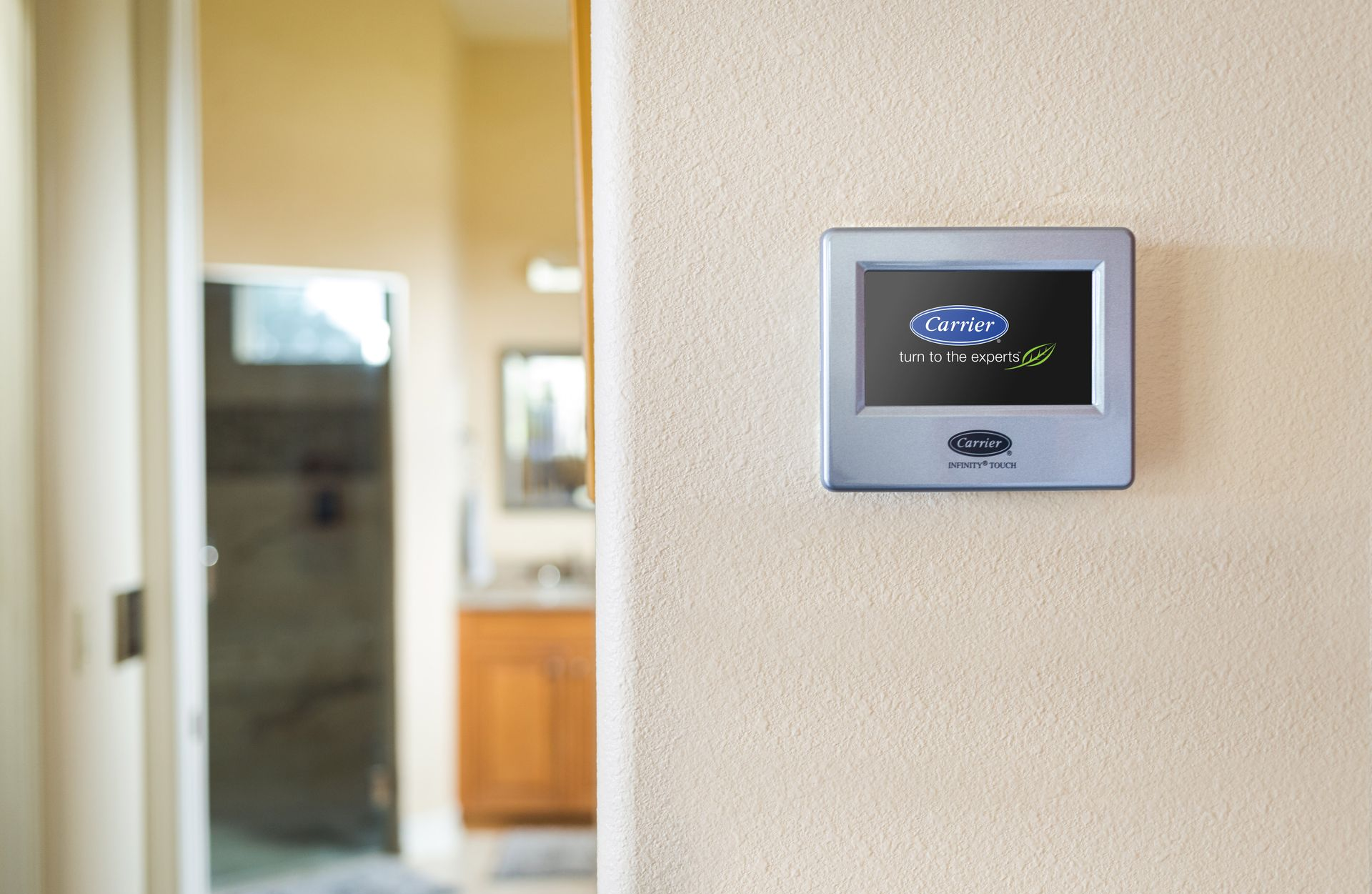 Thermostat on beige wall, bathroom in background. Blue display shows settings.
